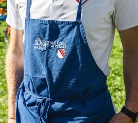 Ein Mann in traditioneller Kleidung hält ein Glas Weißwein und ein Stück Fingerfood in den Händen