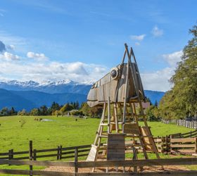 Großes Holzspielgerät in Form eines Pferdekopfs auf einer Wiese mit Bergpanorama im Hintergrund.