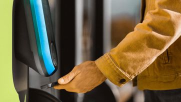 Passenger scans ticket with smartphone at green reader by the door of a bus.