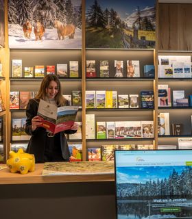 A woman reads a brochure in front of a wall filled with travel leaflets in the tourist office