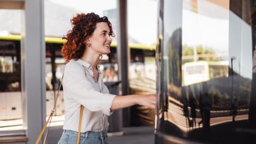 Woman smiling as she boards a green bus at a modern bus stop.